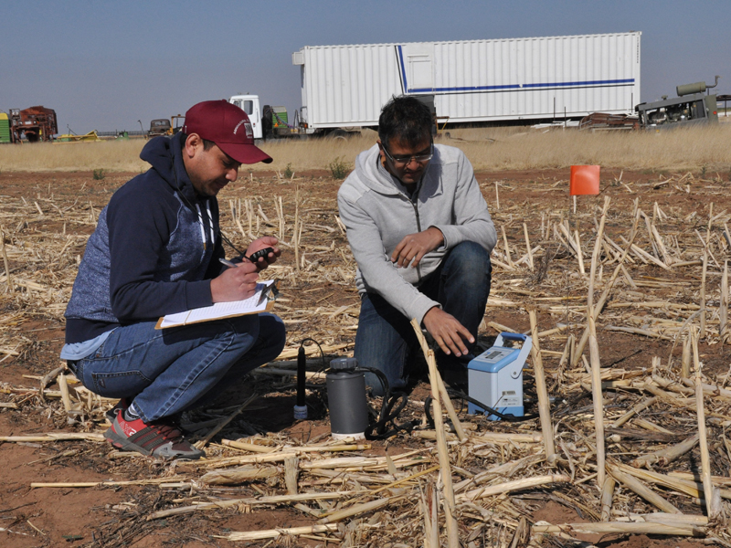 Two men measuring carbon dioxide emissions from soil in field.