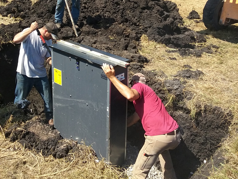 two people putting metal box into hole.