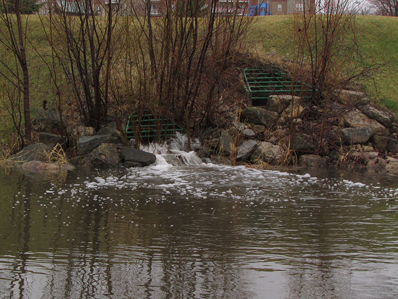 hill with storm drain at bottom and pond with water in it