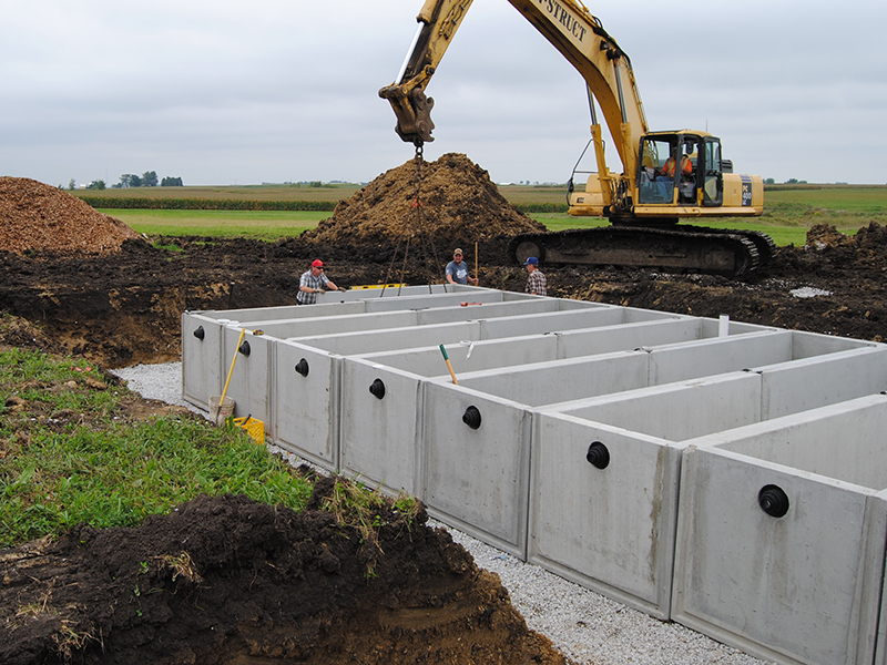 Excavator places concrete barriers in place to line the bioreactor trench in an agricultural field