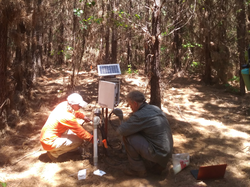 two scientists in forest installing a soil moisture monitoring station