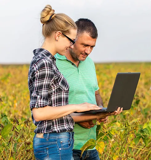 Man and woman standing in a field and looking at a laptop